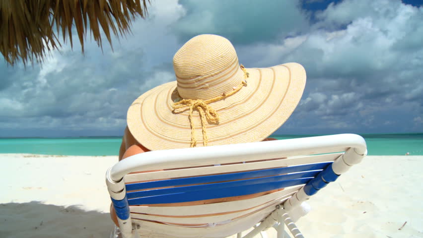 Elegant young female relaxing on white sandy beach looking at aquamarine waters