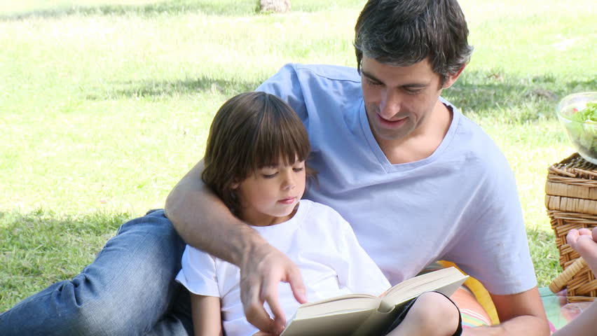 Father and son reading in a park while having picnic with family