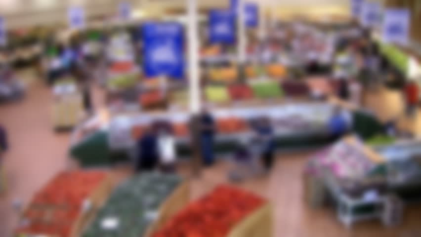 Defocused, "time lapse" shot of modern supermarket. Shoppers in the fruit and vegetable section. Great background to overlay a graphic, logo, or text bar.
