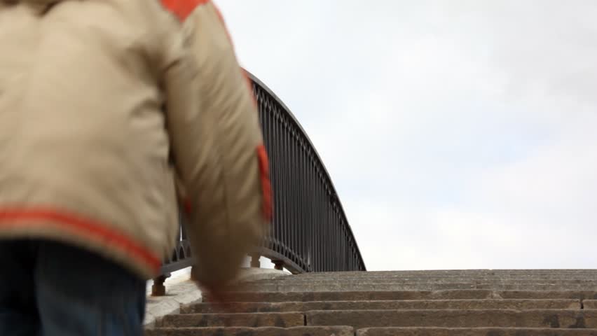 boy runs upwards on steps of stone bridge with an iron handrail 
