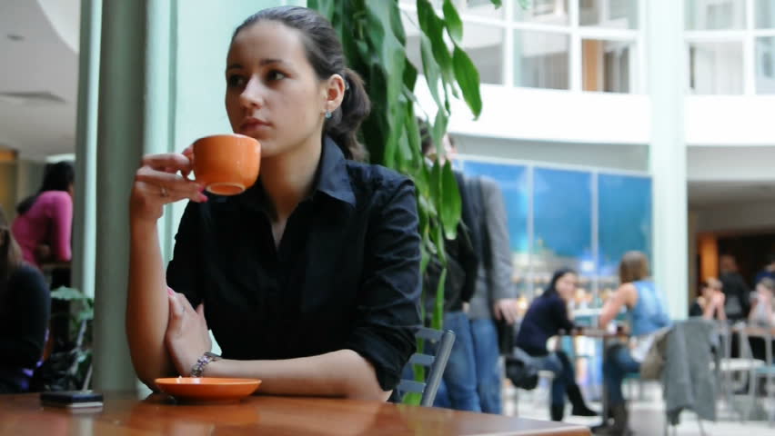 Young woman waiting for someone in a cafe. She is drinking tea and looking around