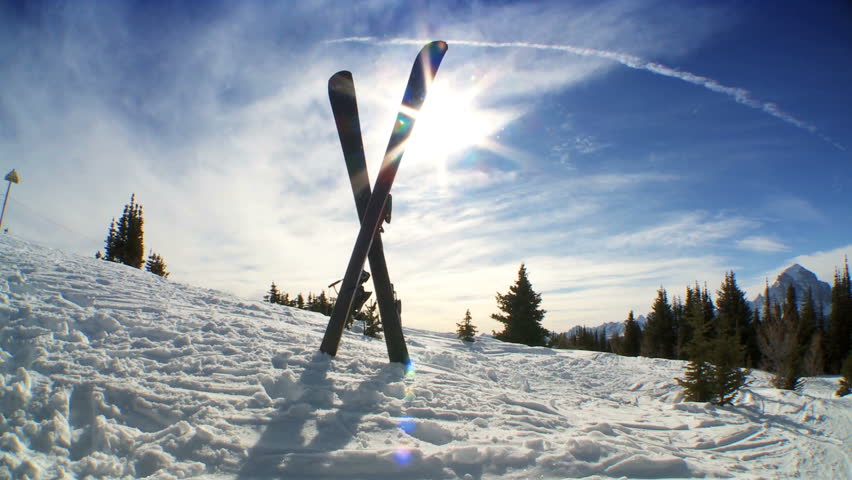 Crossed carver downhill skis & poles standing in fresh clean snow high in scenic mountain landscape