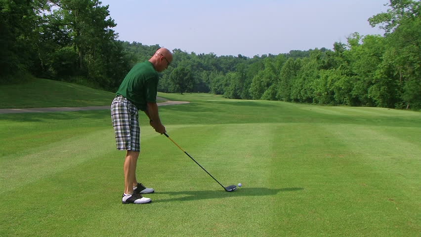 Golfer teeing off with driver onto fairway. 