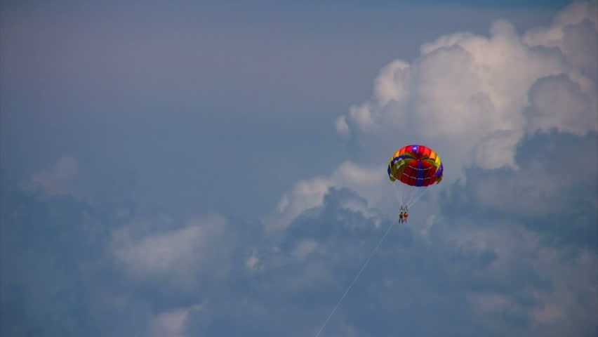 parasailing two humans on coloured parachute flying in sky with clouds 