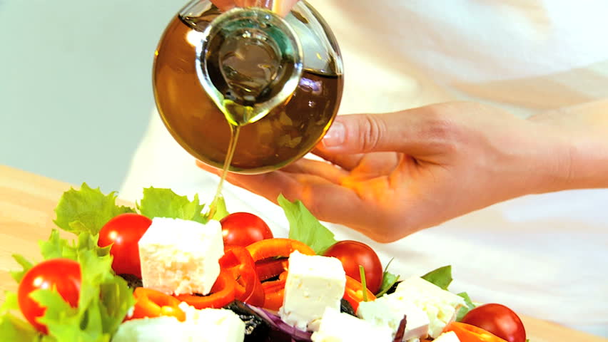 Olive oil being used as a dressing on healthy meal of fresh salad greens, tomatoes & mozarella cheese balls