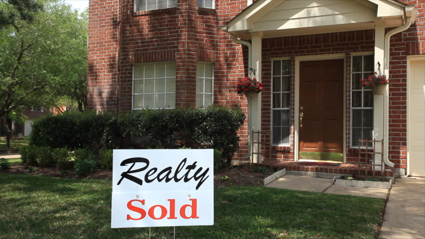 A sign in the front hard of a large brick house advertises that it has been SOLD.