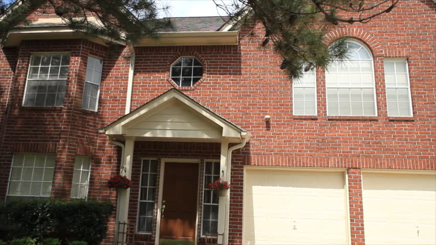 A pleased realtor adds SOLD to a for sale sign that is in front of a large home.