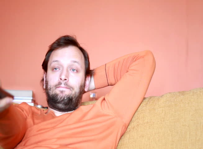 Dolly shot of a bored Man changing channels on tv with remote control - NTSC