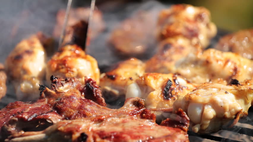 Close-up shot of red meat and chicken legs grilled during picnic 