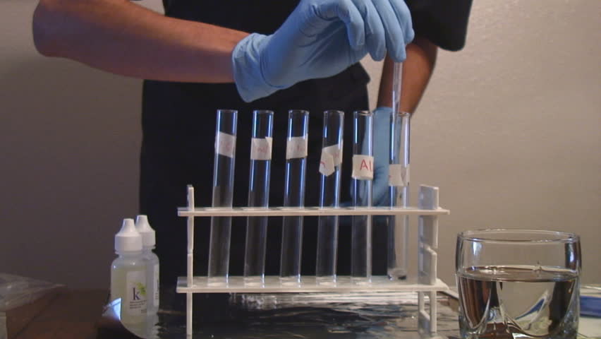 Chemistry student with gloves and goggles performs experiment with chemicals in beakers - HD 