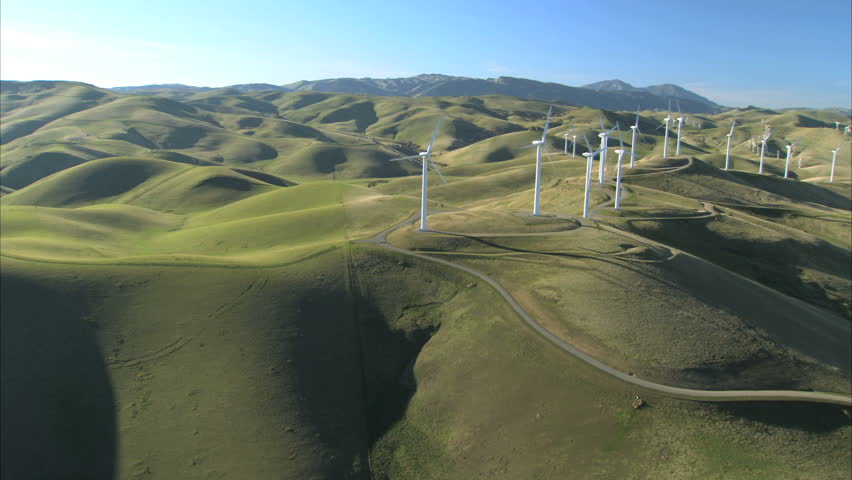 Low aerial view of cluster of wind turbines in green hillside