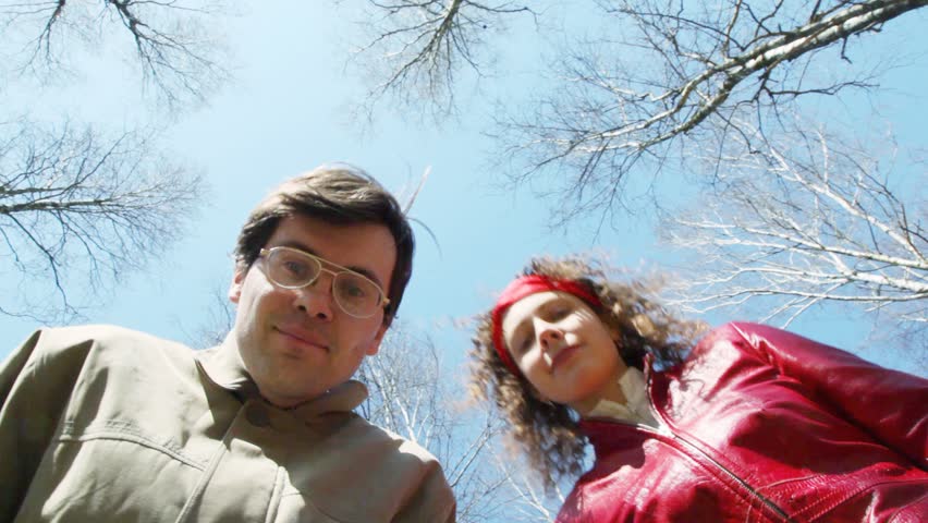 smiling young man and woman looks top-down at camera against spring sky 