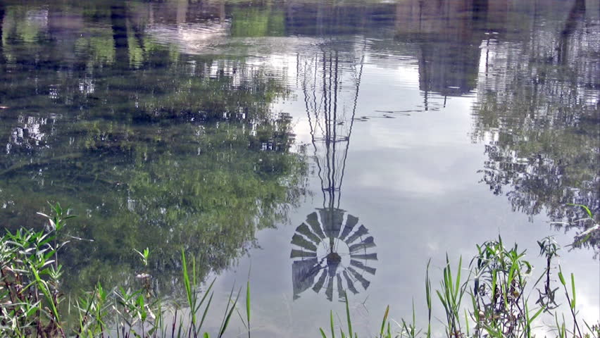 Video of a reflection of a windmill on a south Texas ranch pond. River flowing on farm.  