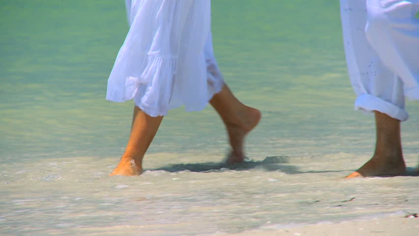 Legs & feet of senior couple walking barefoot through the shallows on the beach 60FPS