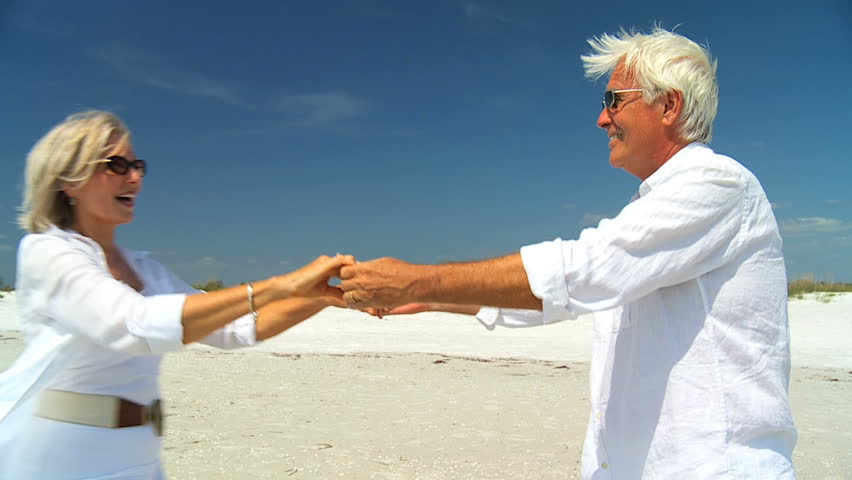 Attractive senior couple dancing on the beach & confidently enjoying a carefree beach lifestyle 60FPS
