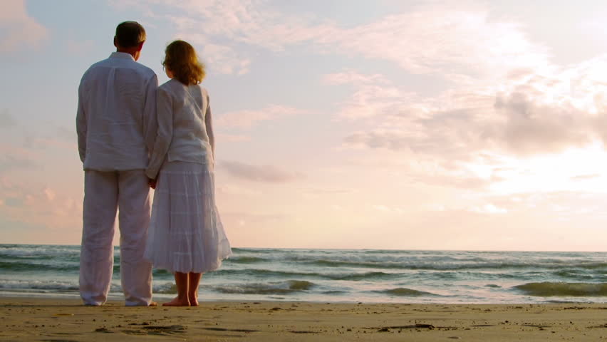 Older couple embrace on the beach while looking into the sunset. 