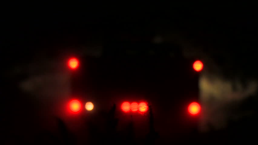 A heavy-duty truck drives away from the camera and into the distance. The truck is off-road and the lights are out of focus.