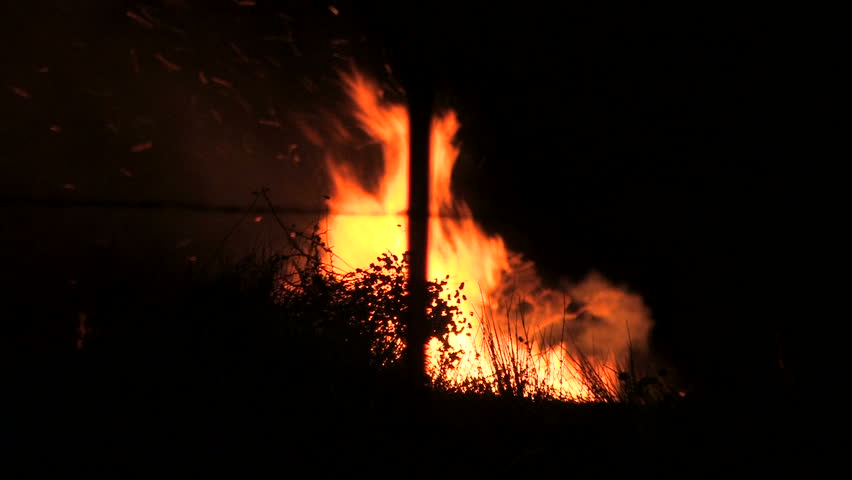 During a California wildfire, brush is consumed by fire. The blaze grows as firemen rush to save homes. You can hear a bulldozer nearby clearing the hillside.