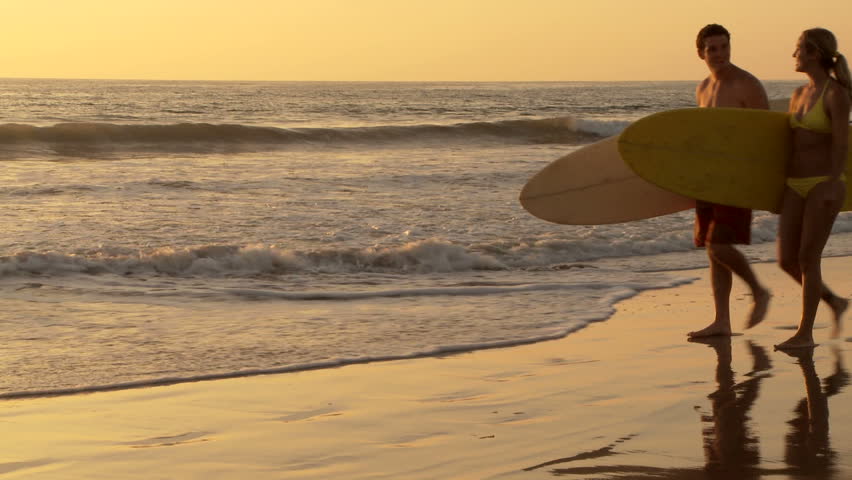Young couple walking with surfboards on beach at sunset