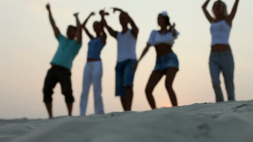 A group of young people dancing on the beach at sunset