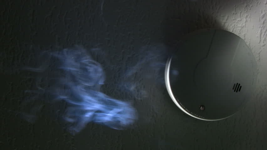 Smoke passes through a ceiling mounted smoke detector causing its activation with flashing red warning light