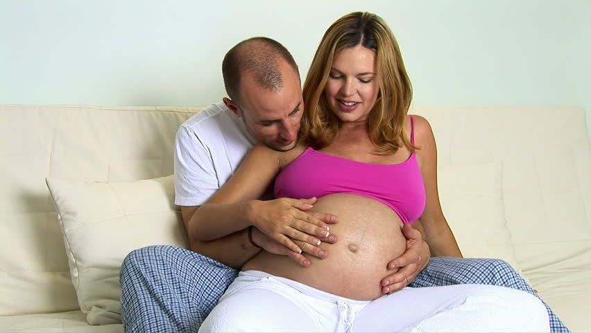 Pregnant couple sitting on couch caressing stomach