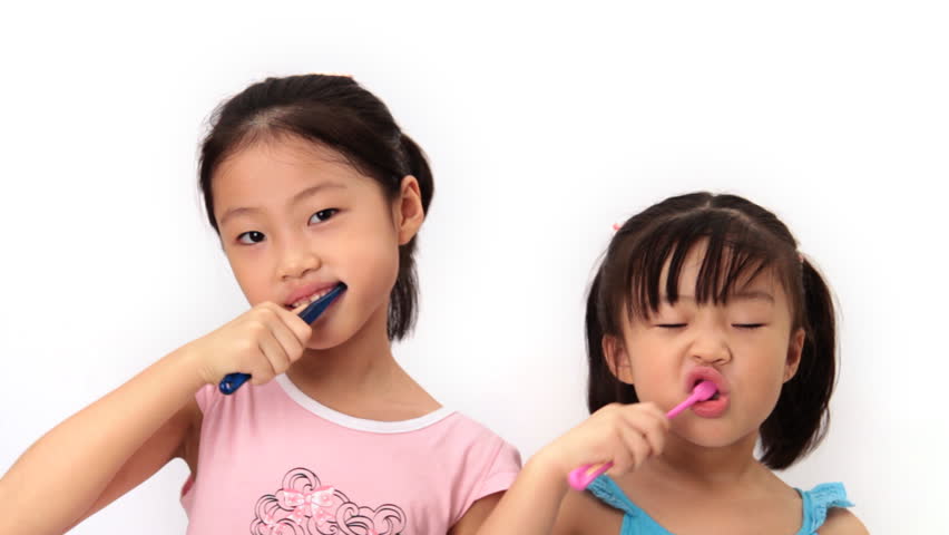 Two sisters look at camera and brush their teeth