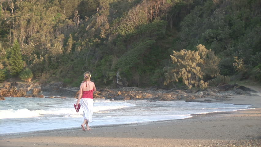 A woman walks alone along a tropical beach at Dusk