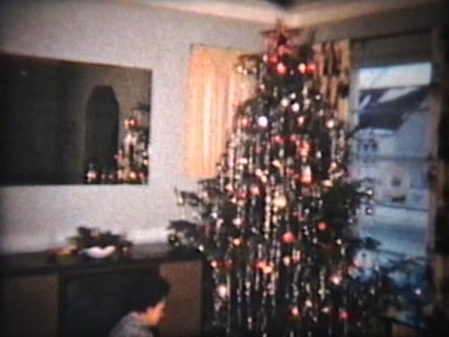 A family spend time together around the Christmas tree opening up gifts and presents to each other.