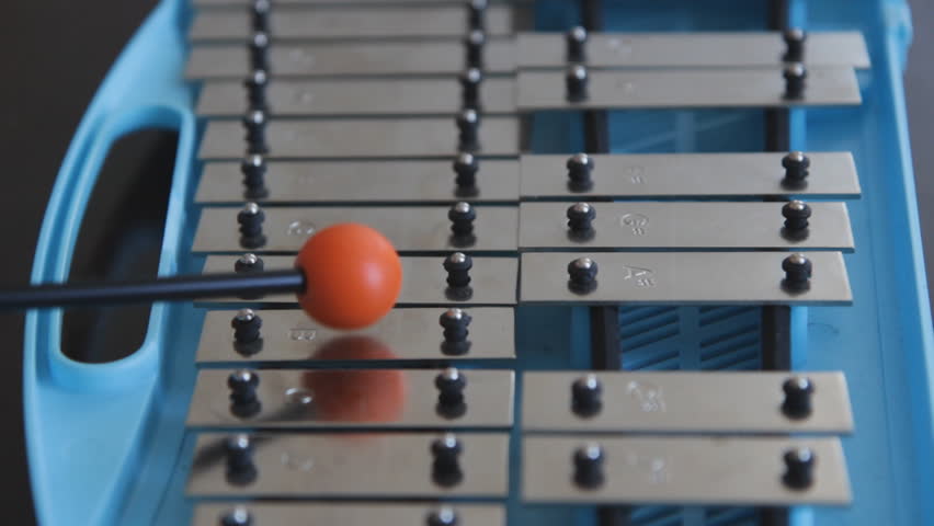 Glockenspiel. Playing a blue children's glockenspiel with an orange rubber mallet. Closeup and shallow DOF.