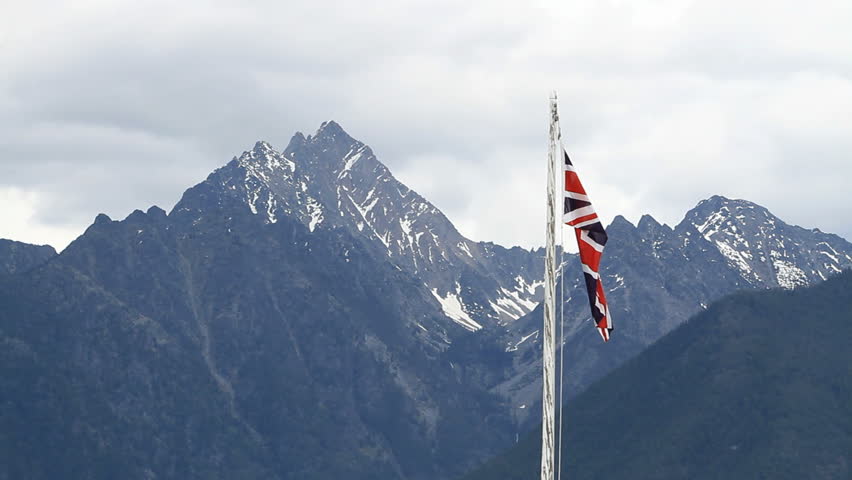 Canadian historic park flies the British Union jack flag on pole in historic Fort Steel, British Columbia, Canada. Banff National Park and glacial snow covered mountains in the distance. 