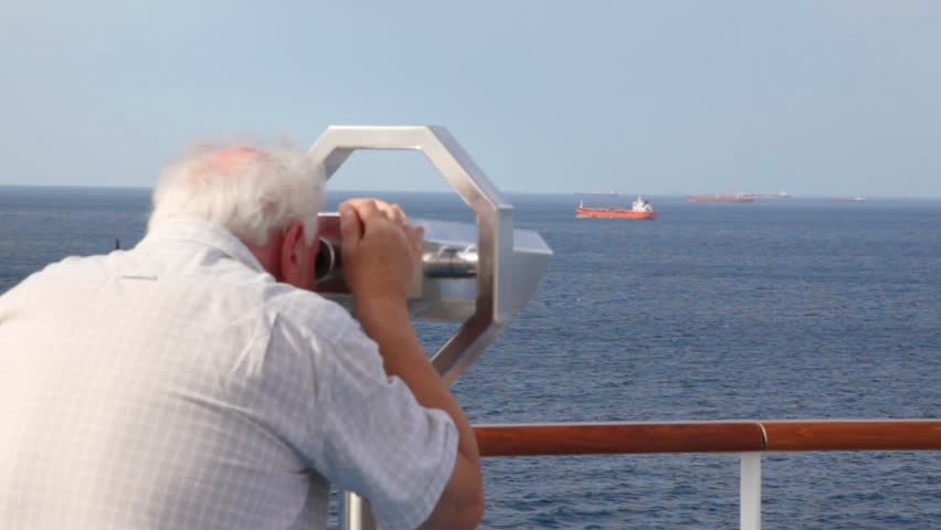 aged man looks through stationary binocular on deck of cruise ship moving in sea