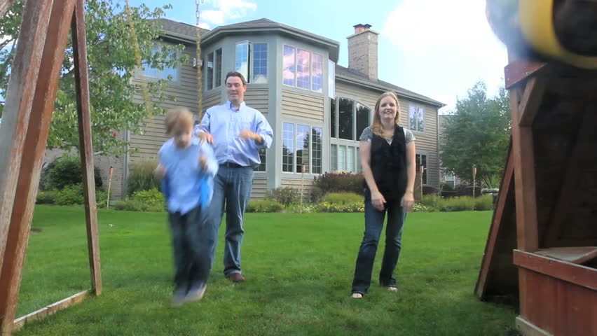 A father and mother push their two kids on the swings in the back yard of their luxury home 