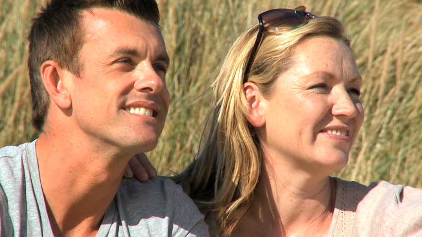 Attractive young caucasian couple enjoying quiet time together sitting in sand dunes at the coast filmed at 60FPS