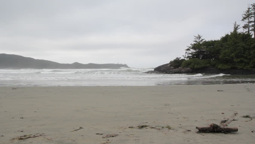 North Pacific beach. View of waves coming in on a cold, grey beach. Coniferous trees on a point. 1080p. Pacific Ocean. Tofino, British Columbia, Canada. 