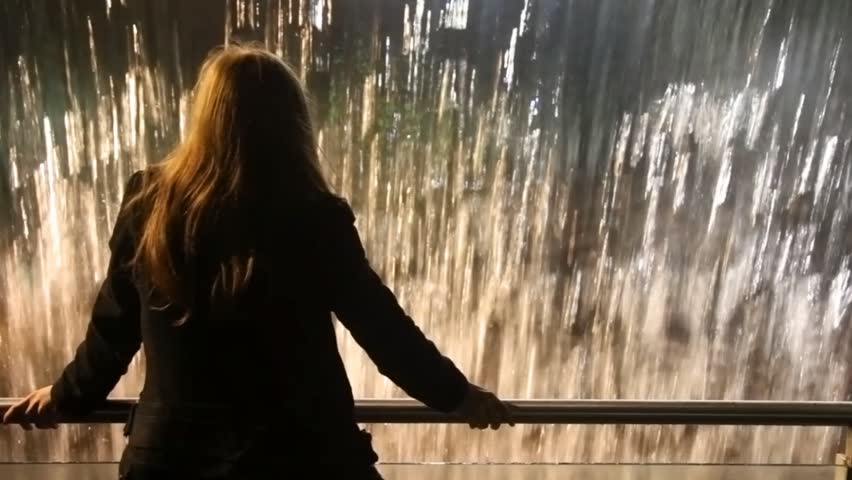 back view of woman standing near railing and looking at artificial waterfall