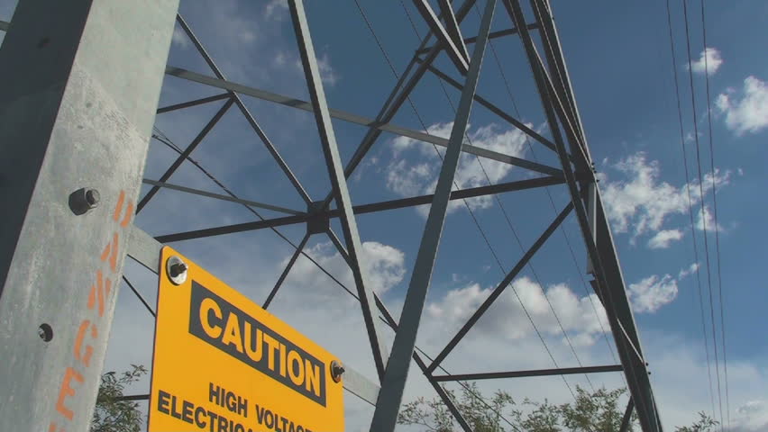 Close up of high voltage caution, danger signs pans upward to wider view of electrical utility tower and wires. 1920x1080