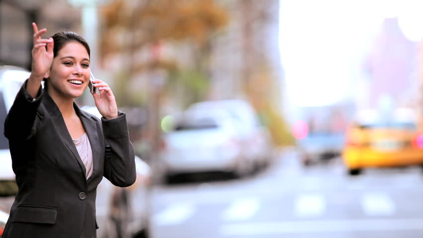 Young female business executive hailing a cab on a busy city street while using her cell phone