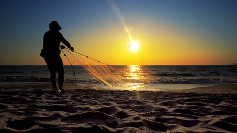 Unrecognizable silhouette fisherman fishing net on the sunset beach; cinematic steadicam shot