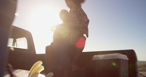 African american woman on mans lap sitting on a pickup truck at beach. They are drinking beer