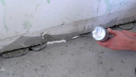 Repair And Construction Work Of The House Worker Man Fills Crack Between Wall And Cement Floor With Mounting Foam In Room Hands Closeup