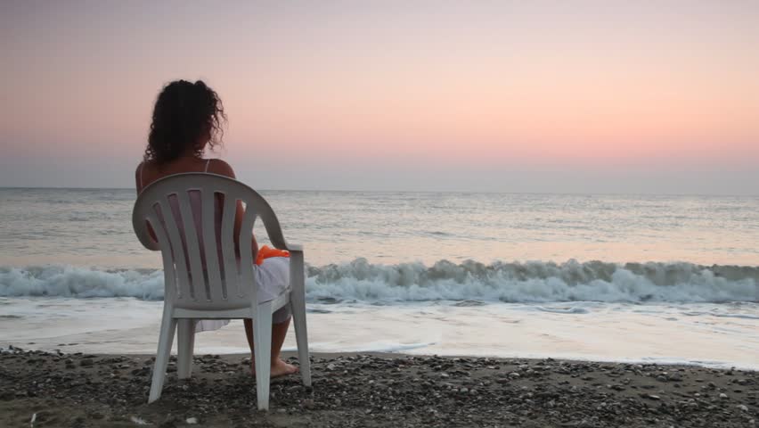 Curlyheaded Woman Sits On White Plastic Chair Alone O