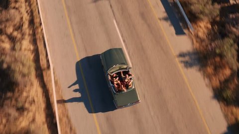 Aerial view of group of road trip friends dancing on the back seat of a retro convertible car