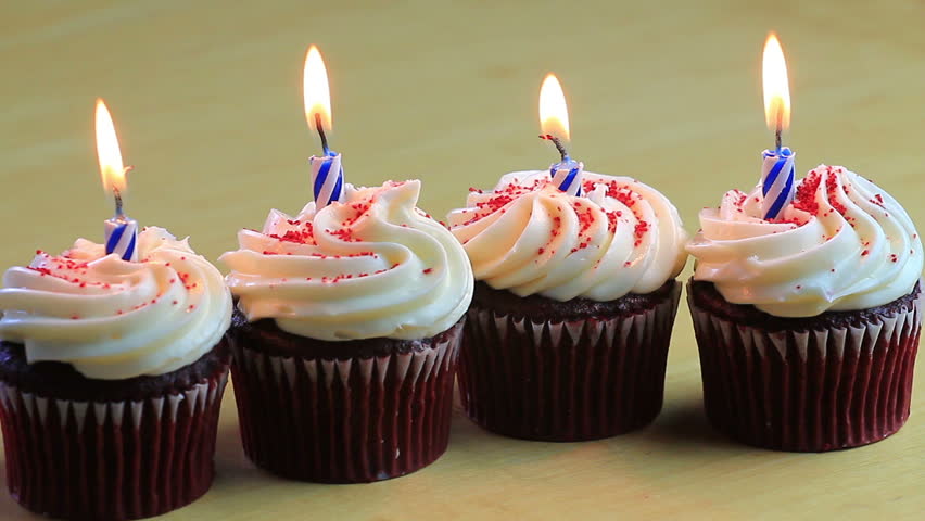 Four Chocolate Birthday Cupcakes With Blue Candles Burning