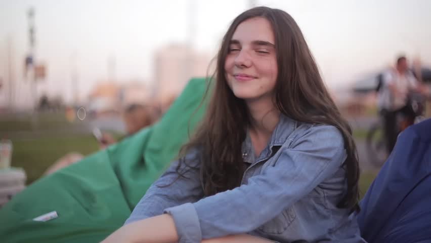 Young Beautiful Teenager Girl In Jeans Jacket Smiling At The Park In Hot Summer Day Sitting In Blue Bean Bag Chair Young Beautiful Teenager Girl In Jeans Jacket Smiling At The Park In Hot Summer Day Sitting In Blue Bean Bag Chair