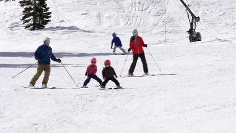 Parents and their children ski to camera together on snowy winter day at Alta Ski Area, Utah.