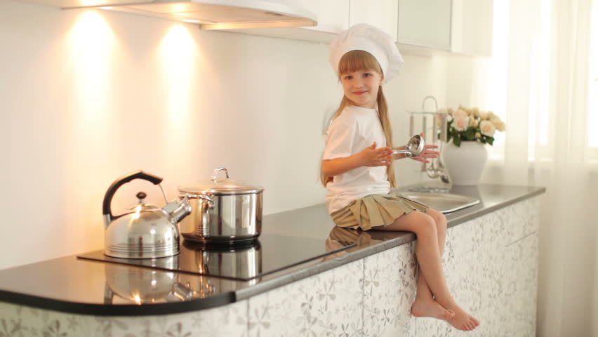 Little Girl Sitting In The Kitchen With A Ladle In Hand