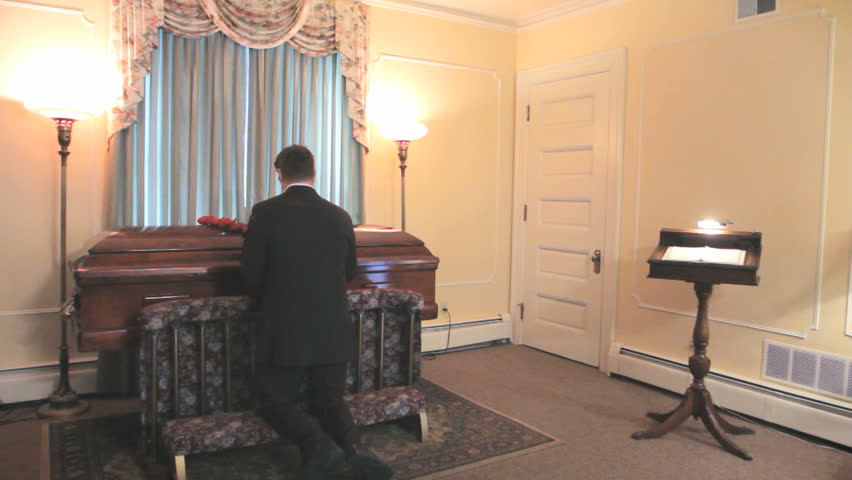 Man Kneels At Coffin At Funeral Home Wake